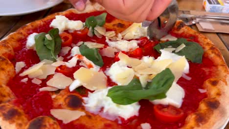 Cortando-Una-Pizza-Italiana-Tradicional-Con-Queso-Burrata,-Queso-Parmesano,-Tomates-Cherry-Y-Albahaca-Fresca,-Tiro-De-4k