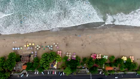 Colorful-umbrellas-on-sandy-beach-of-Kuta-in-Bali-island,-aerial-top-down-view