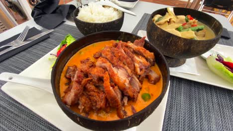 Plato-De-Pato-Crujiente-De-Curry-Rojo-Tailandés-Tradicional-Y-Pollo-Al-Curry-Verde-Con-Arroz-En-Tazones-De-Coco,-Restaurante-De-Cocina-Tailandesa-Sabrosa,-Tiro-De-4k