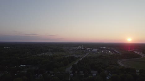 Drohnenaufnahmen-Zeigen-Eine-Kleine-Stadt-In-Ohio,-Umgeben-Von-Bäumen,-Während-Die-Sonne-In-Der-Ferne-Untergeht-Und-Einen-Orangefarbenen-Farbton-Am-Klaren-Himmel-Erzeugt