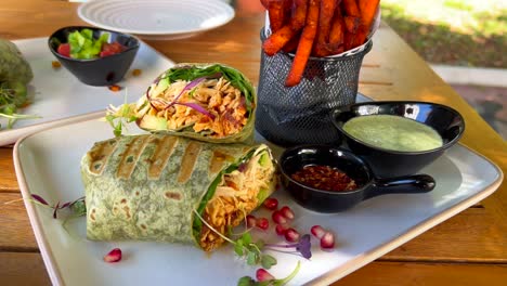 Tasty-chicken-wrap-with-vegetables,-pomegranate,-chili-flakes-and-sweet-potato-fries-in-Marbella-Spain,-enjoying-brunch-during-summer-at-a-restaurant,-4K-shot
