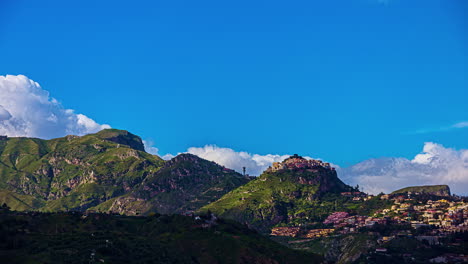 Timelapse-shot-of-floating-clouds-over-a-town-in-a-valley-in-the-mountains-on-a-sunny-day-in-Sicily