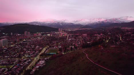 Aerial-orbit-of-the-Andean-mountain-range,-snowy-and-purple-colored-by-the-colors-of-the-sunset,-Las-Condes,-Santiago,-Chile
