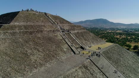 People-climbing-the-stairs-to-the-top-of-the-Temple-of-the-sun,-in-sunny-Teotihuacan,-Mexico---Aerial-view