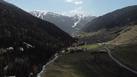 Andorra-valley-and-typical-village-during-summer-season-with-snowy-mountains-in-background,-Pyrenees-in-Spain,-Aerial-rising