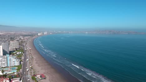 Aerial-orbit-of-La-Serena's-waterfront,-beach-on-a-sunny-day,-Chile