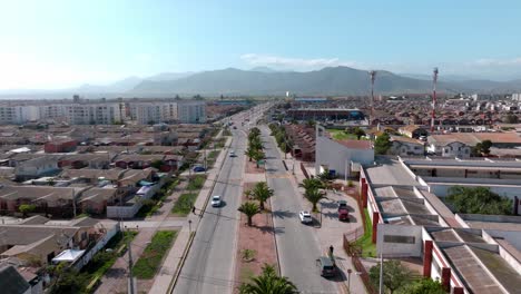 Dolly-in-aerial-view-of-a-road-with-small-palm-trees-in-the-center-and-an-illuminated-mountain-on-a-sunny-day-on-the-horizon,-La-Serena,-Chile