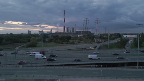 Aerial-view,-camera-approaching-a-coal-fired-power-plant-near-a-busy-highway-with-heavy-traffic