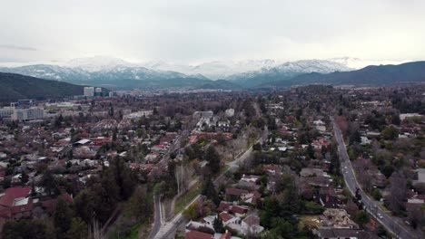 Dolly-in-aerial-view-of-Las-Condes-on-a-cloudy-day-with-the-snowy-Andes-mountain-range-in-the-background,-Santiago,-Chile