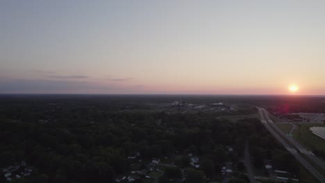 Drohnenaufnahmen-Des-Sonnenuntergangs-Am-Horizont-über-Der-Kleinen-Stadt,-Der-Den-Himmel-Orange-Und-Rosa-Färbt