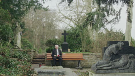 Old-sad-man-sitting-on-bench-in-cemetery,-extreme-wideshot