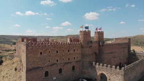 Drone-view-of-Siguenza-Castle,-currently-Parador-tourism,-and-its-Spanish-and-European-flags-waving