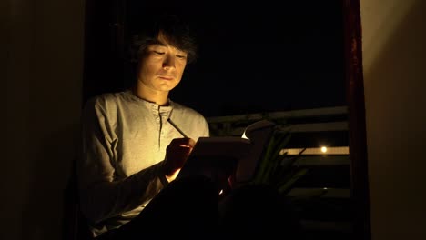 Foto-De-Un-Hombre-Asiático-Leyendo-Un-Libro-En-Una-Habitación-Oscura-Con-Poca-Luz