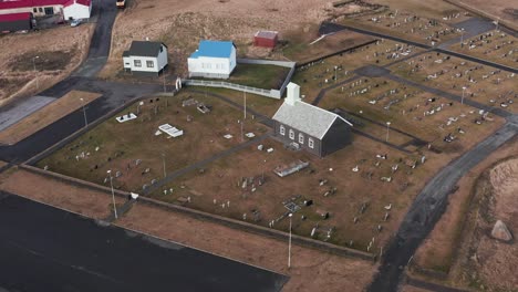Small-local-church-surrounded-with-gravestones-in-Iceland,-aerial
