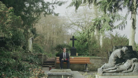 Sad-man-sitting-on-bench-in-cemetery,-extreme-wide-shot