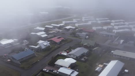 Residential-buildings-in-Njardvik-village-with-thick-fog-clouds,-aerial