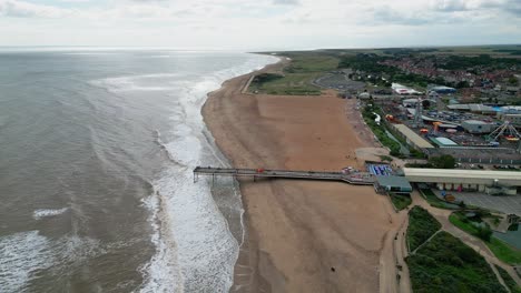 Typical-English-seaside-resort,-shot-using-a-drone,-giving-a-high-aerial-viewpoint-showing-a-wide-expanse-of-sandy-beach-with-a-pier,-crashing-waves-and-fun-park