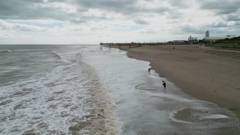 Typical-English-seaside-resort,-shot-using-a-drone,-giving-a-high-aerial-viewpoint-showing-a-wide-expanse-of-sandy-beach-with-a-pier-and-crashing-waves-9