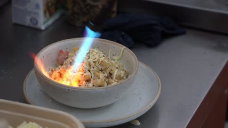 Handheld-motion-close-up-shot-of-professional-chef-torch-a-bowl-delicious-and-tasty-macaroni-and-cheese,-adults-and-kids-favourite-comfort-food