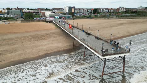 Typical-English-seaside-resort,-shot-using-a-drone,-giving-a-high-aerial-viewpoint-showing-a-wide-expanse-of-sandy-beach-with-a-pier-and-crashing-waves-6