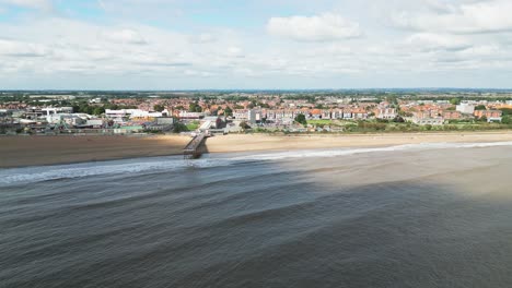 Typical-English-seaside-resort,-shot-using-a-drone-flying-into-the-sun-giving-a-aerial-viewpoint-with-a-wide-expanse-of-beach-with-a-pier-and-crashing-waves-2