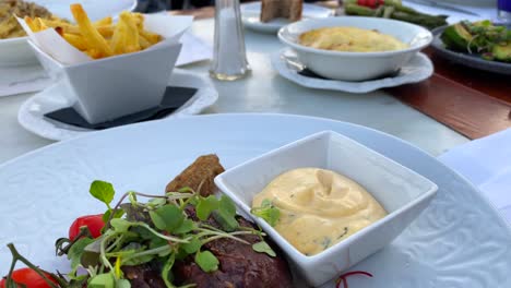 Juicy-fillet-steak-with-bearnaise-sauce,-salad-and-french-fries-at-a-restaurant-table-with-food,-big-family-dinner,-4K-shot