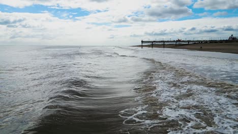 English-tourist-seaside-resort,-shot-using-a-drone,-giving-a-high-aerial-viewpoint-showing-a-wide-expanse-of-sandy-beach-with-a-pier-and-crashing-waves