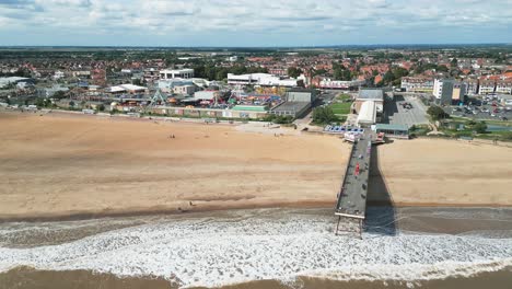 Very-popular-English-seaside-resort,-shot-using-a-drone,-giving-a-high-aerial-viewpoint-showing-a-wide-expanse-of-sandy-beach-with-a-pier-and-crashing-waves