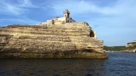 Low-angle-view-from-sea-of-famous-Madonnetta-lighthouse-built-on-rock-in-Southern-Corsica-island-seen-from-sailing-touristic-boat