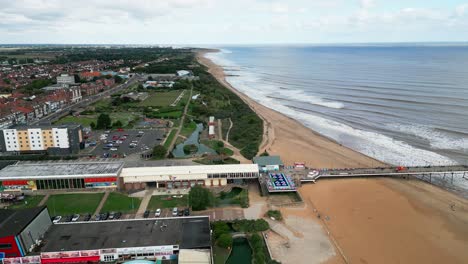 Typical-English-seaside-resort,-shot-using-a-drone,-giving-a-high-aerial-viewpoint-showing-a-wide-expanse-of-sandy-beach-with-a-pier-and-crashing-waves-4
