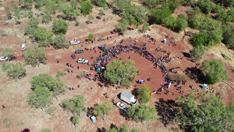 Drone-view-of-people-at-the-cermony-site-at-the-end-of-the-Freedom-Day-Festival-march,-panning-up-with-the-community-of-Kalkaringi-in-the-background