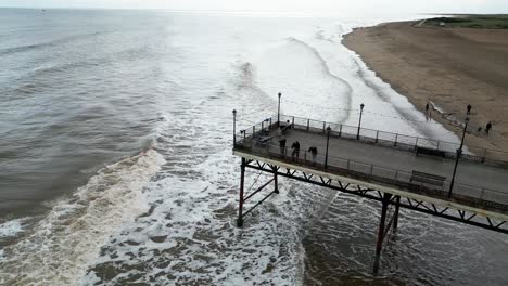 Typical-English-seaside-resort,-shot-using-a-drone,-giving-a-high-aerial-viewpoint-showing-a-wide-expanse-of-sandy-beach-with-a-pier-and-crashing-waves-1