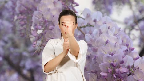 Sportswoman-in-kung-fu-uniform-practicing-wing-chun-kung-fu-punches-with-wisteria-flowers-in-background