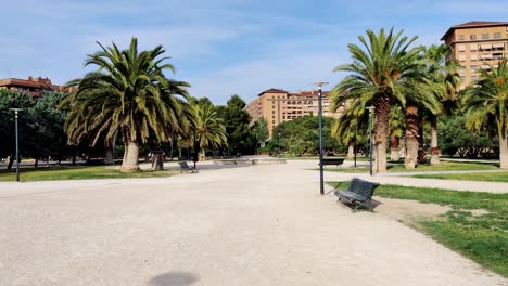 Tropical-park-with-palm-trees-and-cityscape-in-Zaragoza,-slow-motion-view