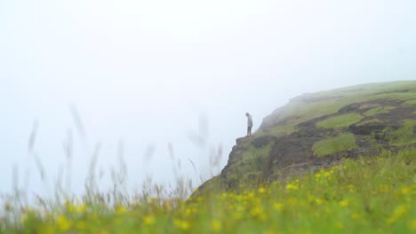 Distant-View-Of-A-Hiker-On-The-Edge-Of-A-Cliff-In-A-Misty-Sunrise