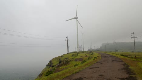 Straße-Zwischen-Windkraftanlagen-Und-Strommasten-An-Einem-Nebligen-Morgen