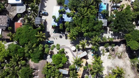Cars-driving-and-people-walking-on-beach-road-in-Tulum-Hotel-zone-on-sunny-day,-static-aerial-to-down