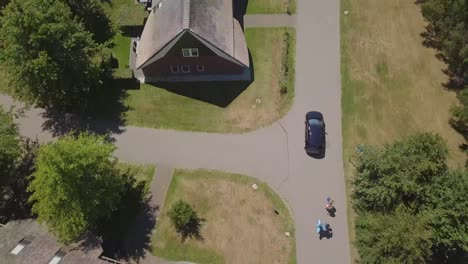 Zenital-drone-shot-of-a-dark-blue-car-driving-on-a-road-with-houses-next-to-it,-in-the-Netherlands