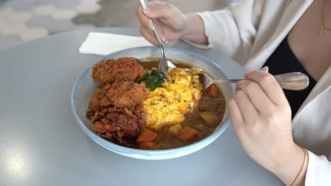 Young-female-lady-digging-in-a-bowl-of-delicious-Japanese-omurice-with-curry-sauce-and-crispy-buttermilk-fried-chicken,-handheld-motion-close-up-shot