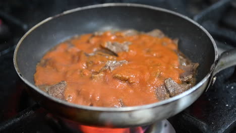 Adding-the-tomato-sauce-to-the-stir-fried-beef-strips-in-a-saucepan-on-the-gas-stove,-preparation-of-Turkish-kebab