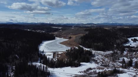 Flying-over-forest-in-early-spring-with-mountains-on-background