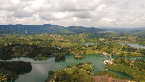 Panoramic-Guatape-Medellin-Colombia-Antioquia-Aerial-Drone-Above-Lake-Cloudy-Day-Crystalline-Water-and-Green-Hills-Zoom-Out-Piedra-del-PeÃ±ol