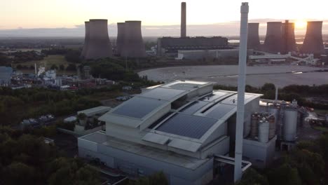 Aerial-panning-right-view-across-smart-solar-rooftop-factory-with-sunrise-emerging-from-behind-fossil-fuel-power-station