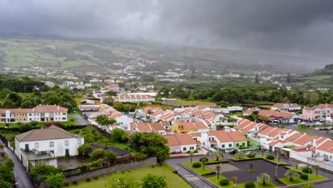Small-hillside-town-in-Azores-below-dark-storm-clouds,-aerial-view