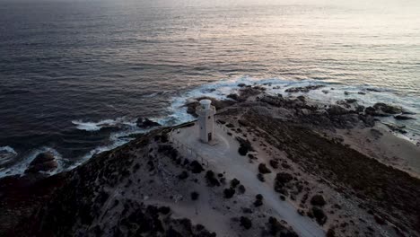 Aerial-ascending-motion,-Lighthouse-Silhouette-at-rocky-coast,-Cape-Spencer-during-Sunset