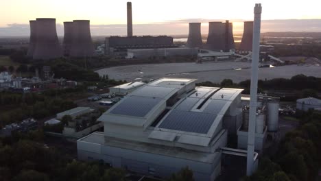 British-smart-solar-rooftop-factory-with-sunrise-emerging-from-behind-fossil-fuel-power-station-aerial-panning-right-view
