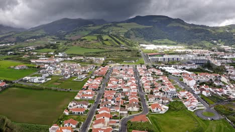 Storm-forming-over-mountains-above-coastal-town-in-Azores,-aerial-view