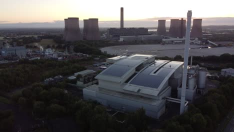 Morning-aerial-rising-view-above-smart-UK-solar-rooftop-factory-and-fossil-fuel-power-station-at-sunrise