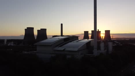 Sunrise-emerging-behind-silhouette-of-power-station-stacks-and-British-solar-energy-factory-aerial-descending-view