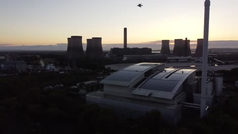 Sunrise-aerial-view-orbiting-modern-UK-solar-rooftop-factory-and-fossil-fuel-power-station-skyline